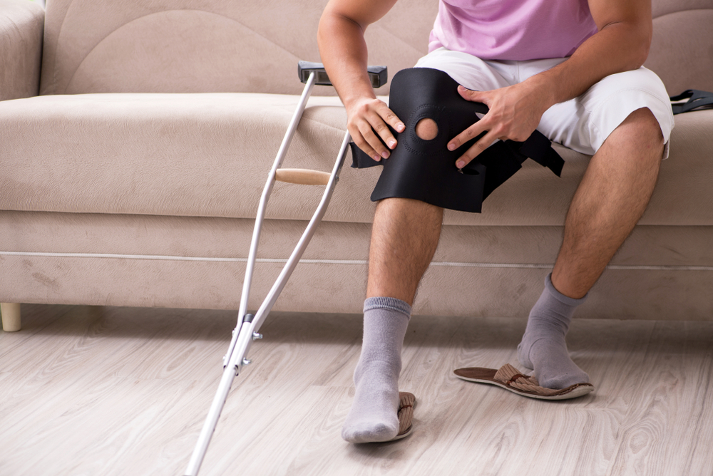 Injured man covering his knee with crutches beside him